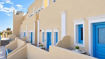 Una hilera de habitaciones de hotel con balcones, cada una con una puerta azul y molduras blancas.