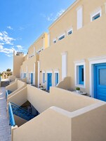 Una hilera de habitaciones de hotel con balcones, cada una con una puerta azul y molduras blancas.