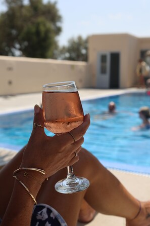 Une personne tenant un verre contenant une boisson près d’une piscine.