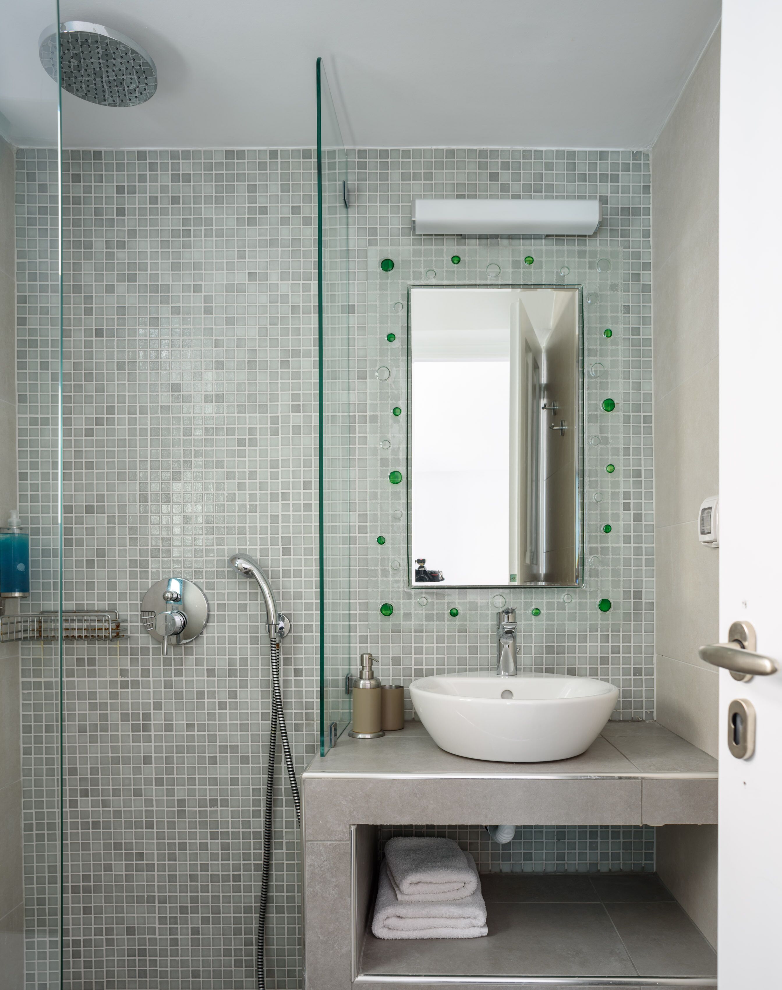 A modern bathroom with a glass shower enclosure, a white sink, and a mirror with green decorative elements.