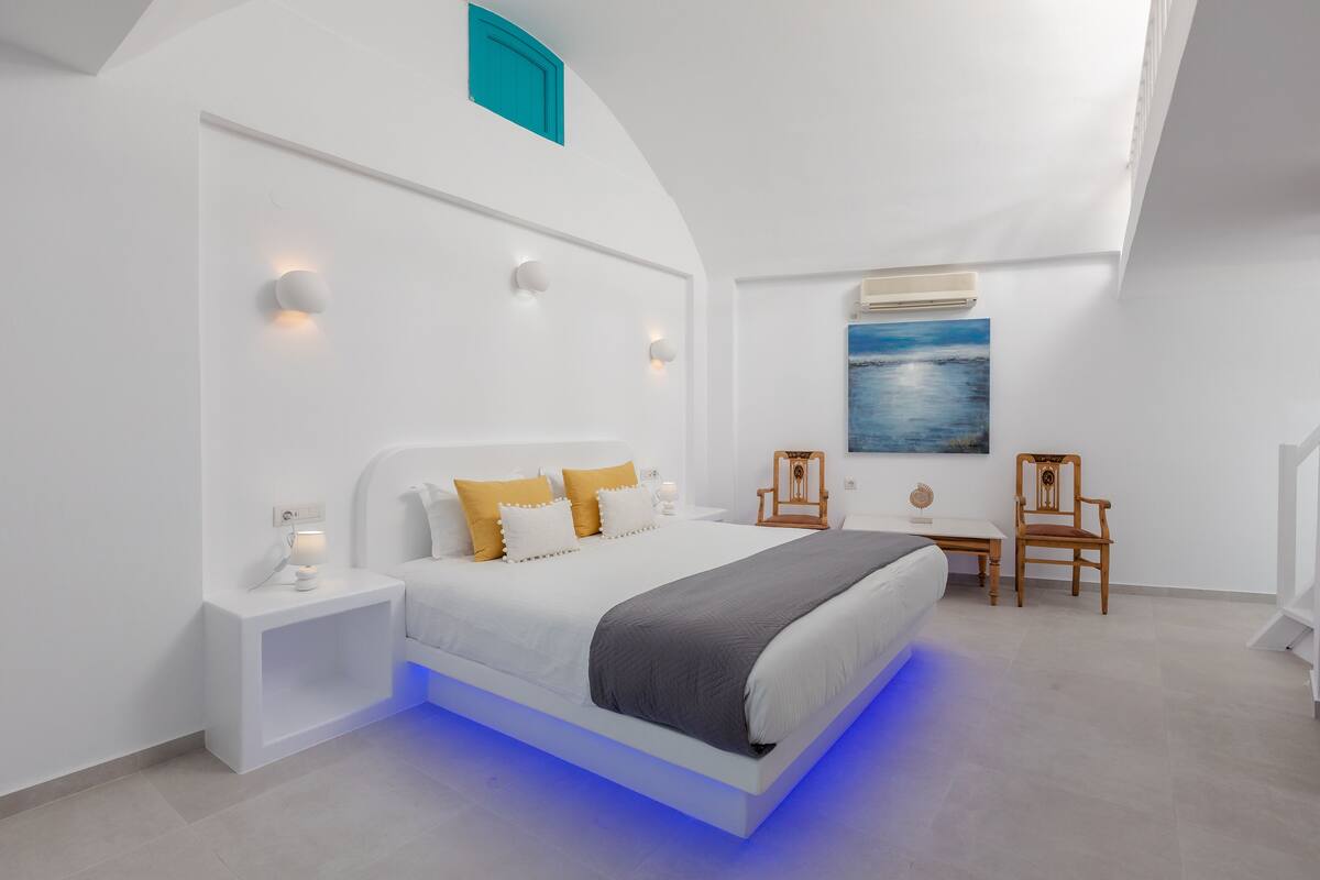 A modern bedroom with a bed, bedside tables, a chair, and a painting on the wall.