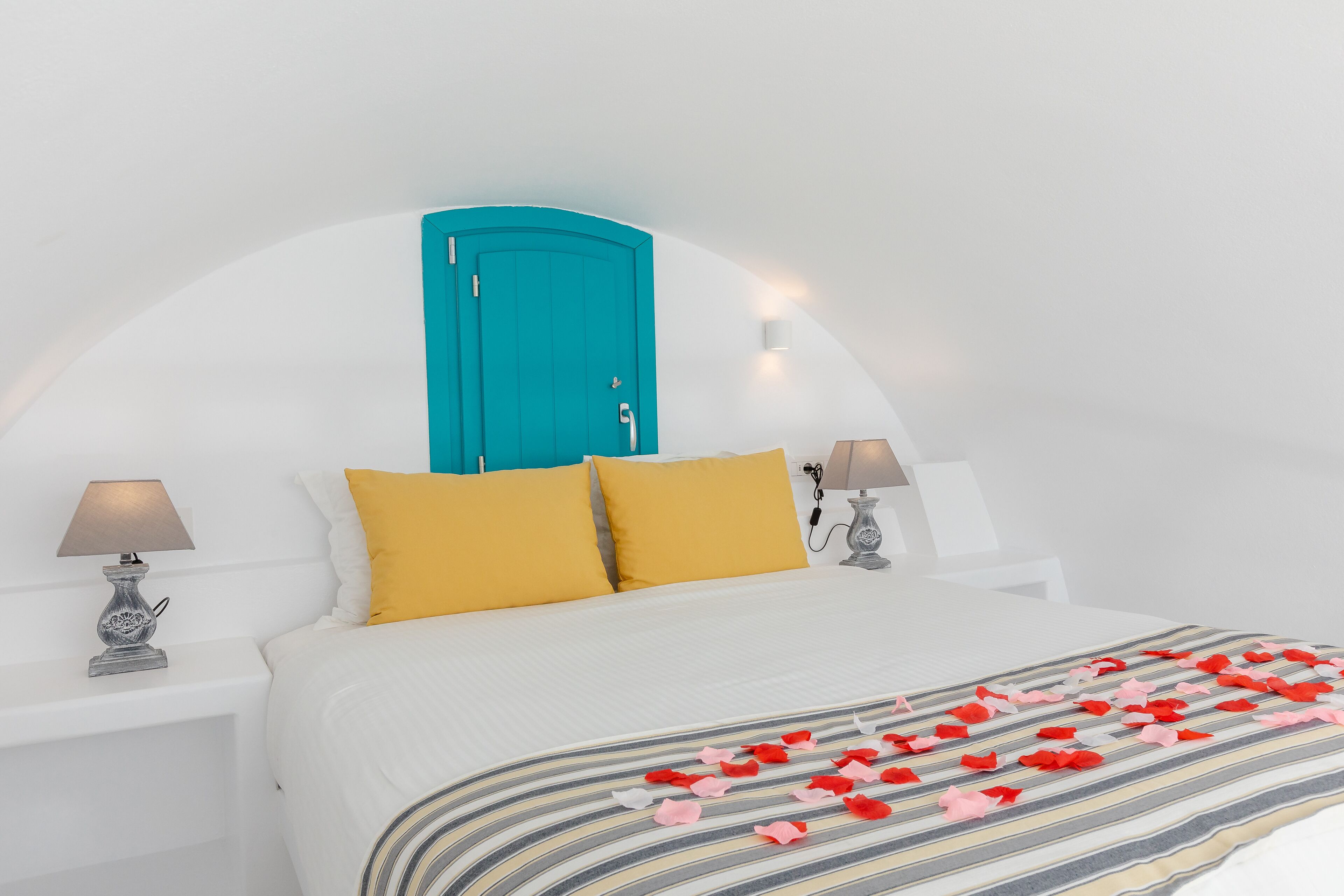 Un dormitorio con una cama, un armario azul turquesa, dos lámparas de noche y una colcha a rayas con pétalos de rosa.