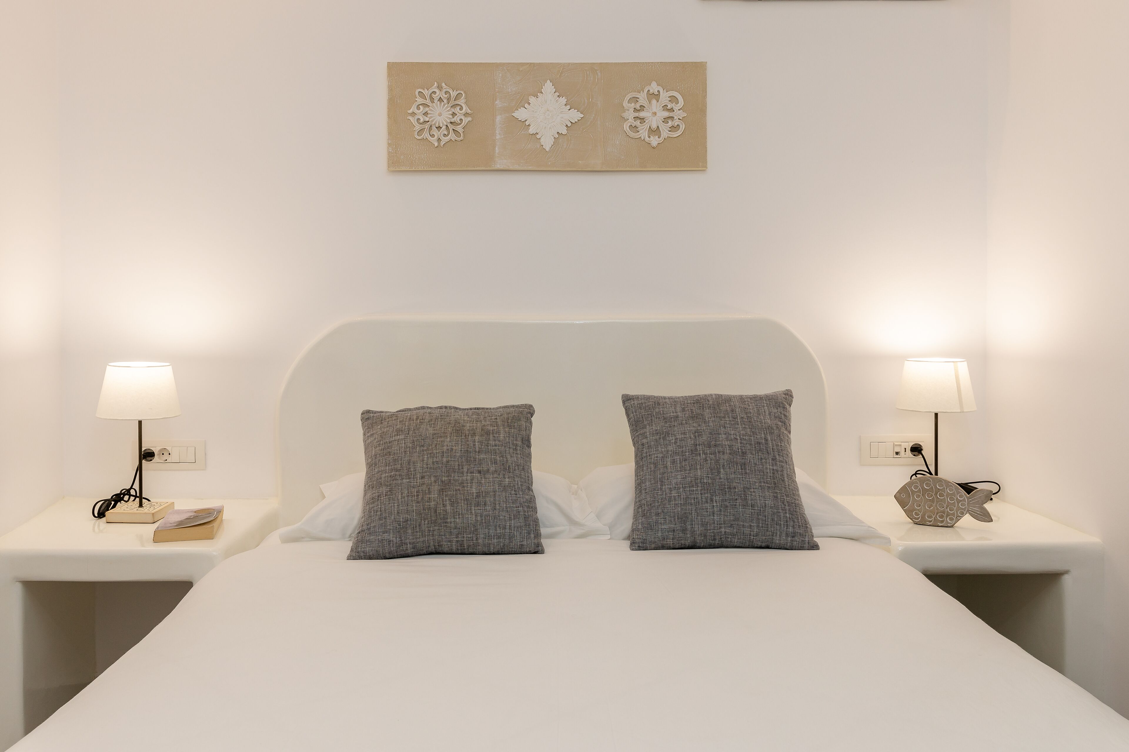 A neatly made bed with two pillows, two bedside tables with lamps, and a decorative wall piece above the bed.