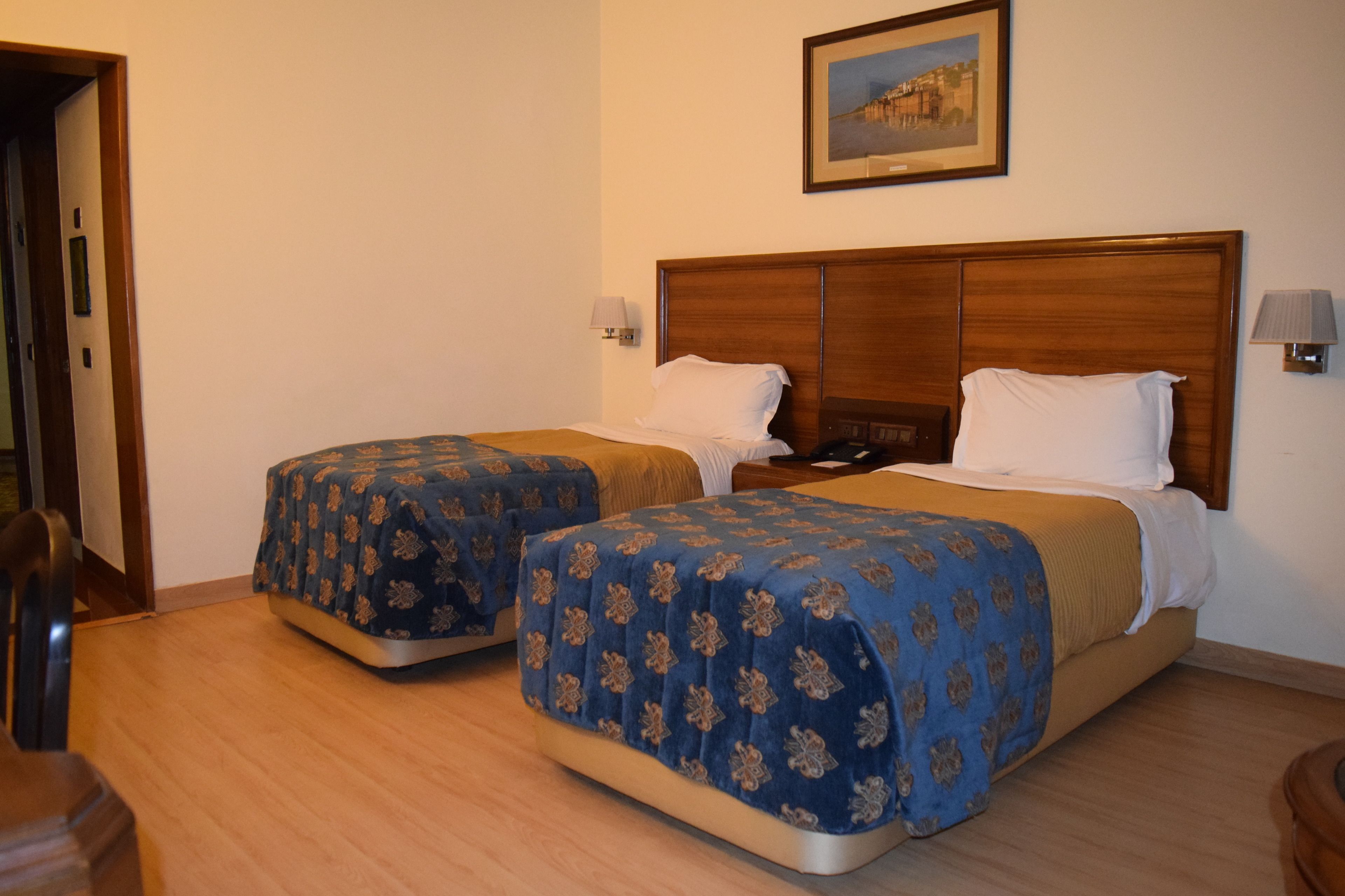 A hotel room with two beds, wooden headboards, and a painting on the wall.