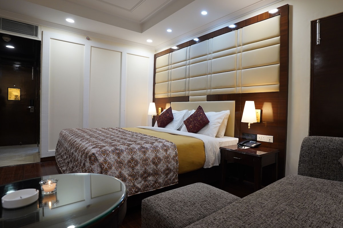 A hotel room with a large bed, bedside tables, a desk, and a sofa.