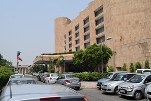 A parking lot with several cars parked in front of a large building with multiple floors and a flat roof.