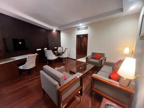 A modern hotel lobby with a wooden reception desk, a dining area with a round table and chairs, and a seating area with sofas and armchairs. - Hotel Samrat (New Delhi)