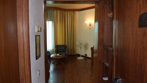 Un couloir avec un plancher en bois, un ventilateur, une chaise et une table.
