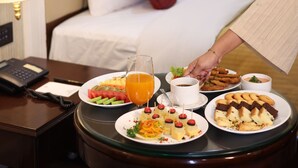 Une chambre d’hôtel avec un lit, une table de chevet avec une lampe et un plateau de petit-déjeuner contenant divers aliments et boissons.