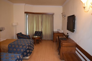 A hotel room with two beds, a desk, a chair, a lamp, a television, and a window with curtains.