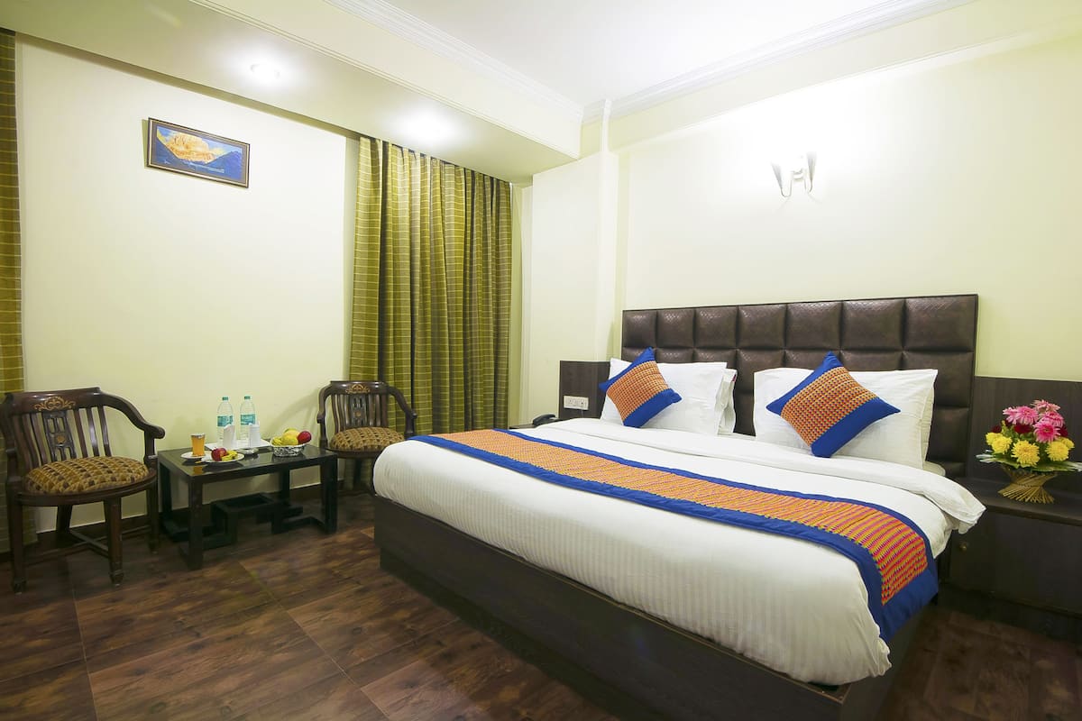 Ein Hotelzimmer mit einem großen Bett, zwei Sesseln, einem kleinen Tisch mit Obstschale und einem Nachttisch mit Blumenvase.