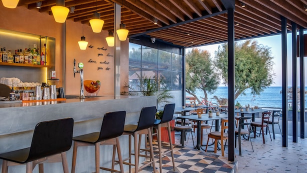 A bar area with stools, a counter with bottles, and a view of the sea.