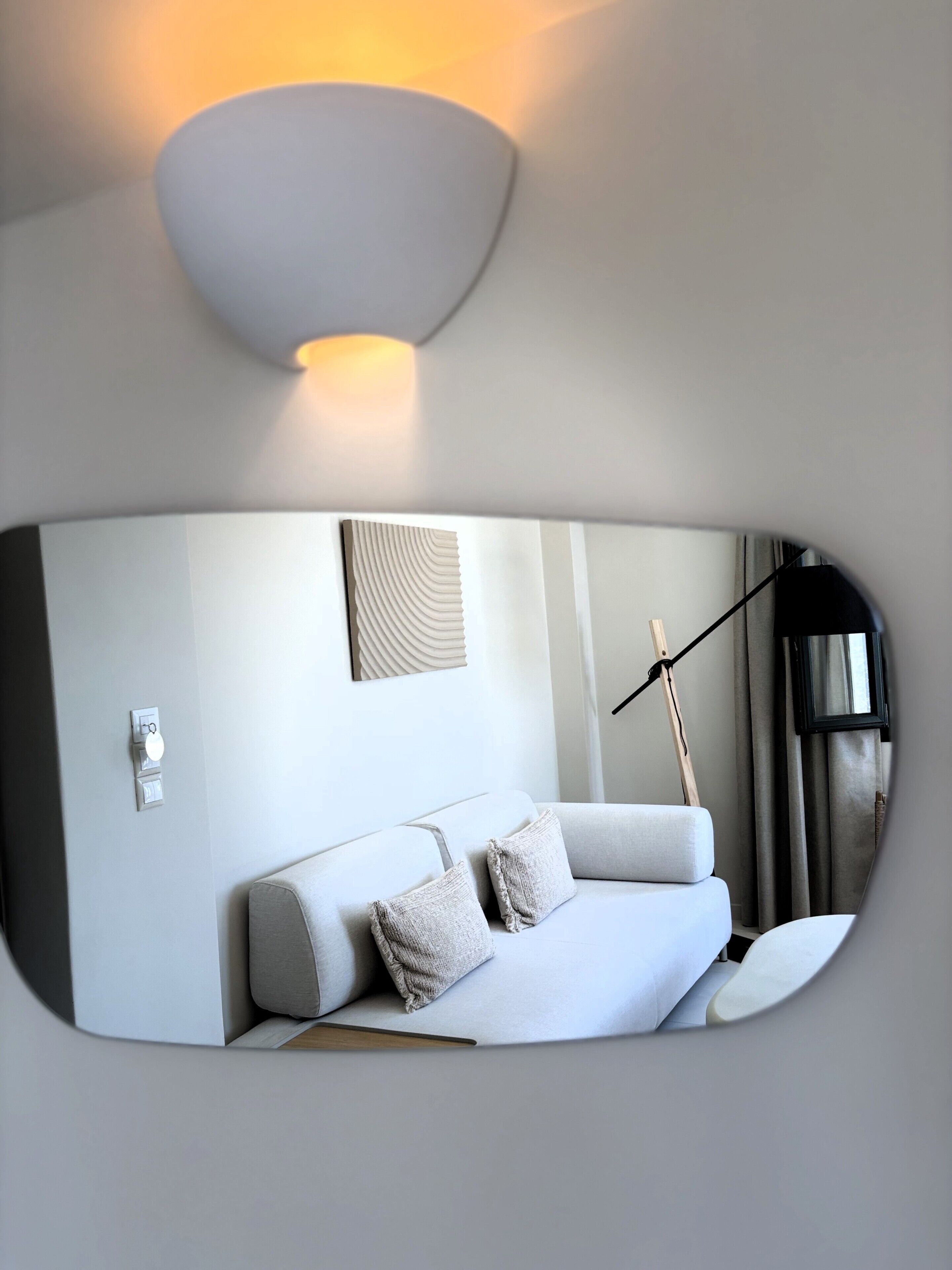 Un intérieur moderne avec un canapé, un luminaire fixé au mur et un miroir qui reflète la pièce.