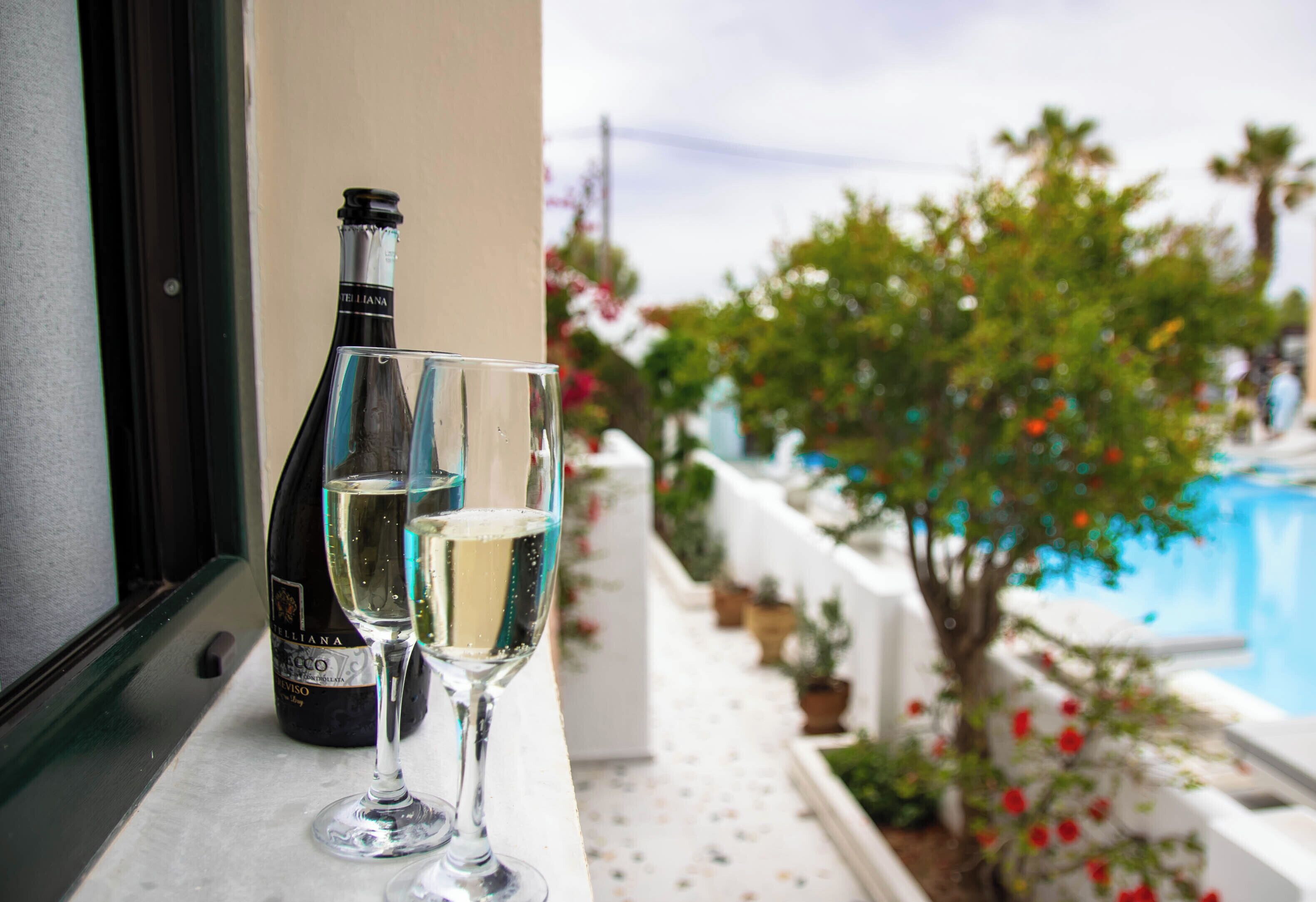 A bottle of wine and a glass on a balcony with a pool view.