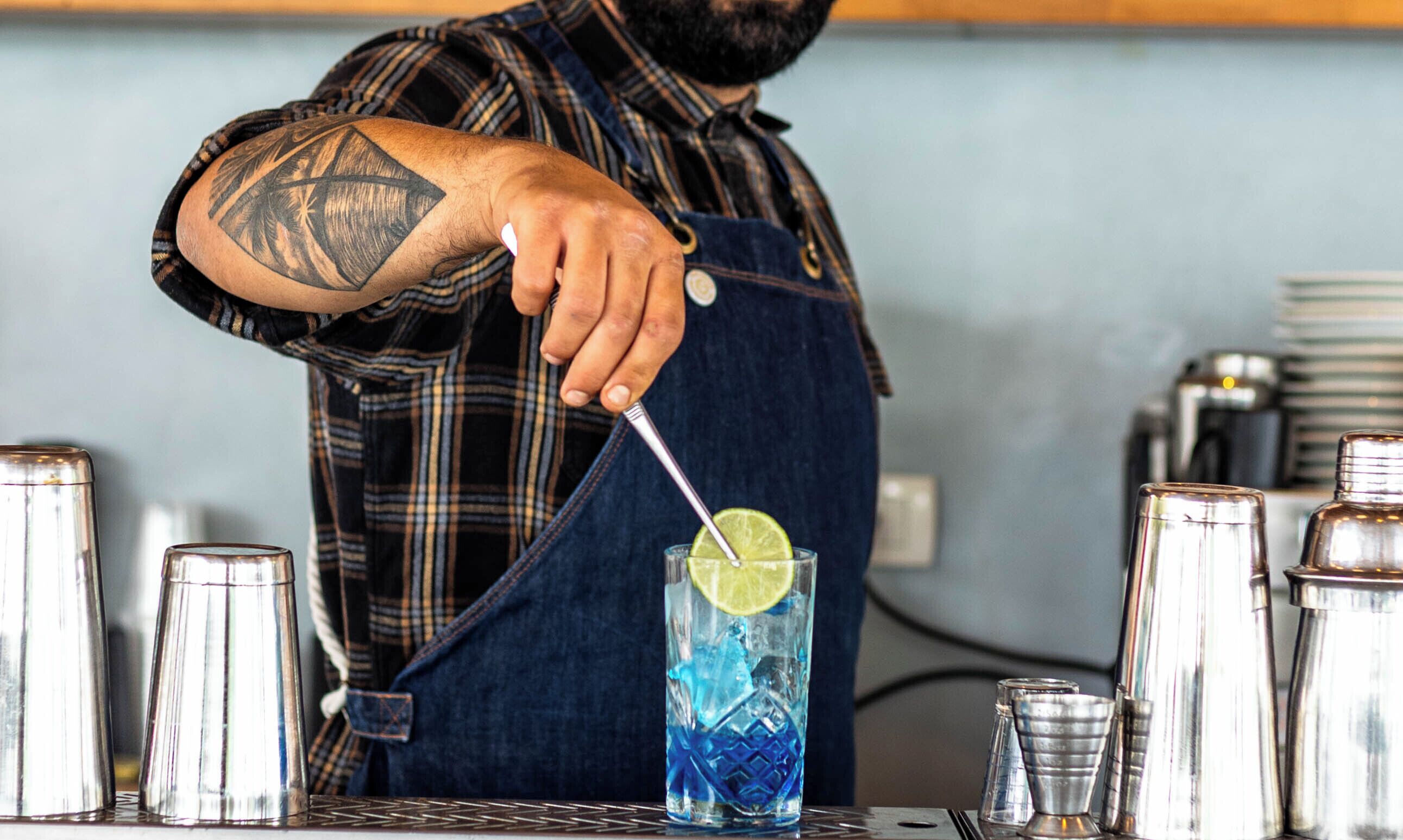 Un barman prépare un cocktail dans un grand verre, en y ajoutant une tranche de citron vert.