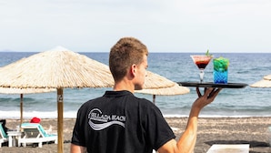 A beach scene with a person holding a tray with two drinks.