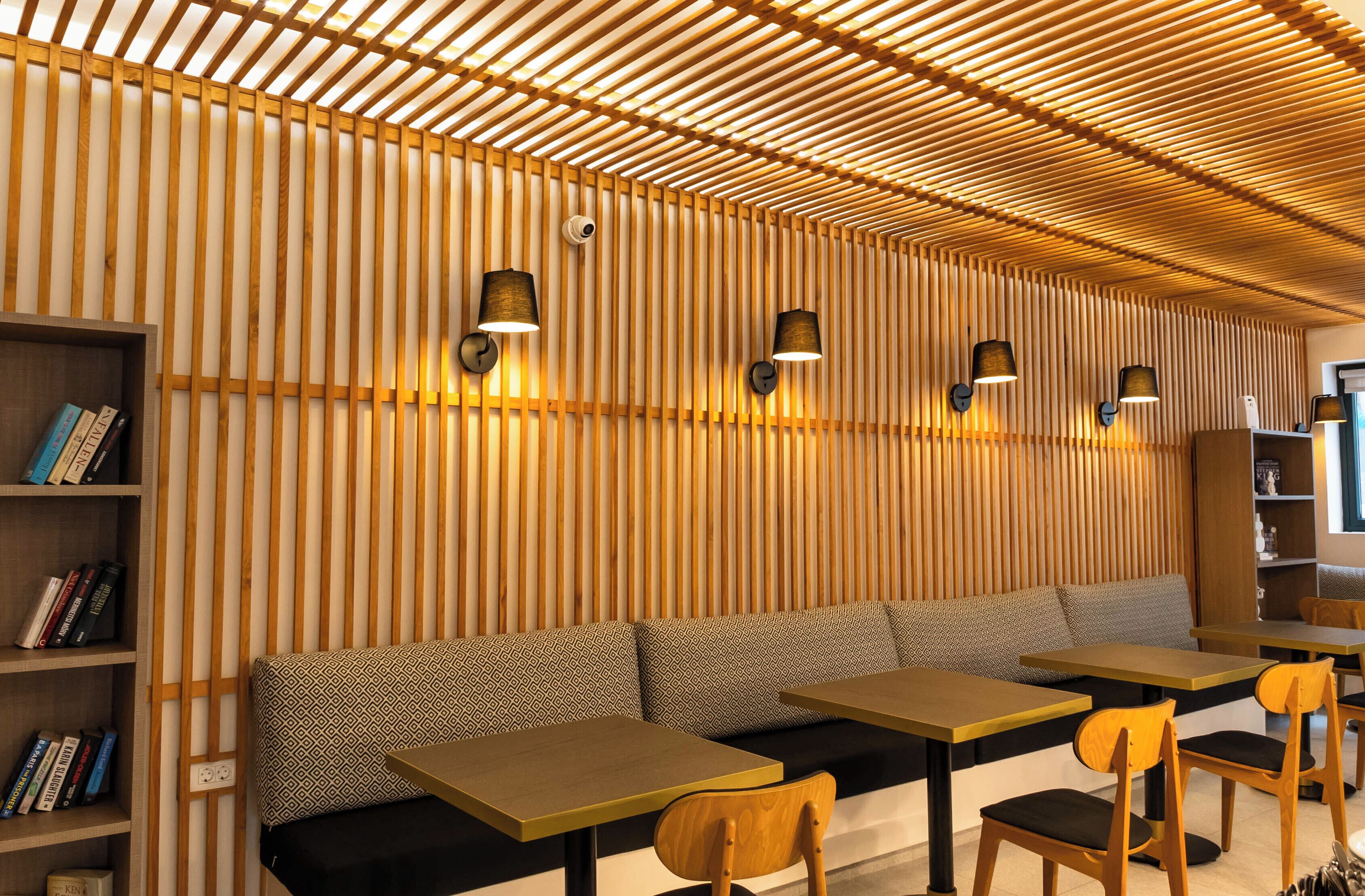 Un interior moderno con listones de madera en el techo, un sofá con cojines estampados y mesas con sillas.