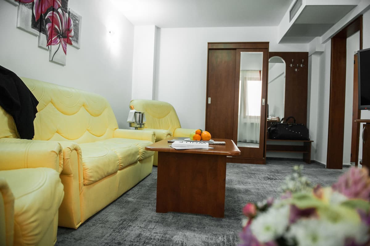 A yellow sofa, a wooden coffee table, a mirror, and a television in a room with a grey carpet.