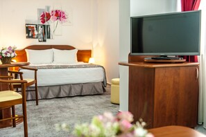 A hotel room with a bed, a TV on a wooden stand, a desk with a chair, and a small table with flowers. - Hotel Parc Sibiu (Sibiu)