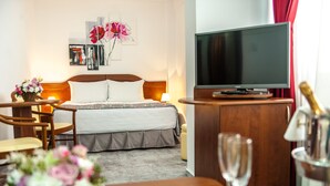 A hotel room with a bed, a television, a wooden desk, a chair, a vase of flowers, and a champagne glass. - Hotel Parc Sibiu (Sibiu)