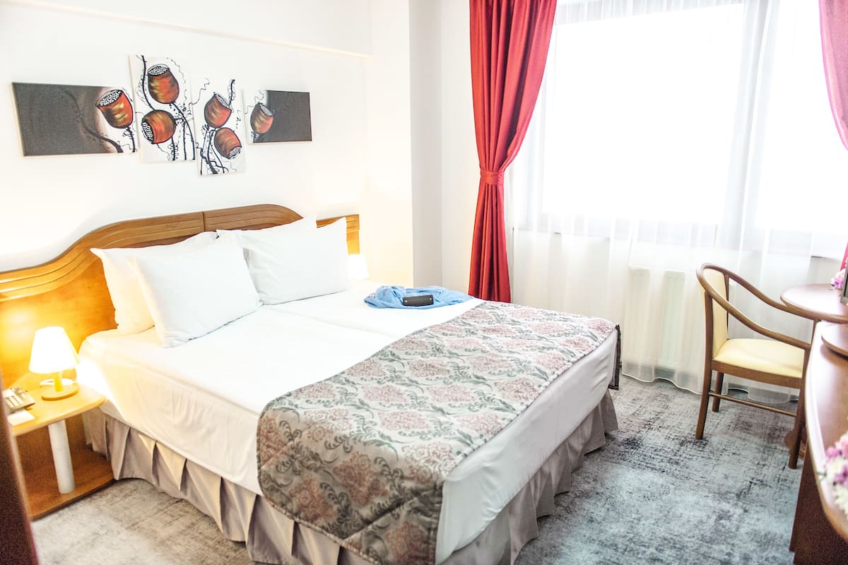 A hotel room with a bed, a bedside table with a lamp, a chair, and artwork on the wall.