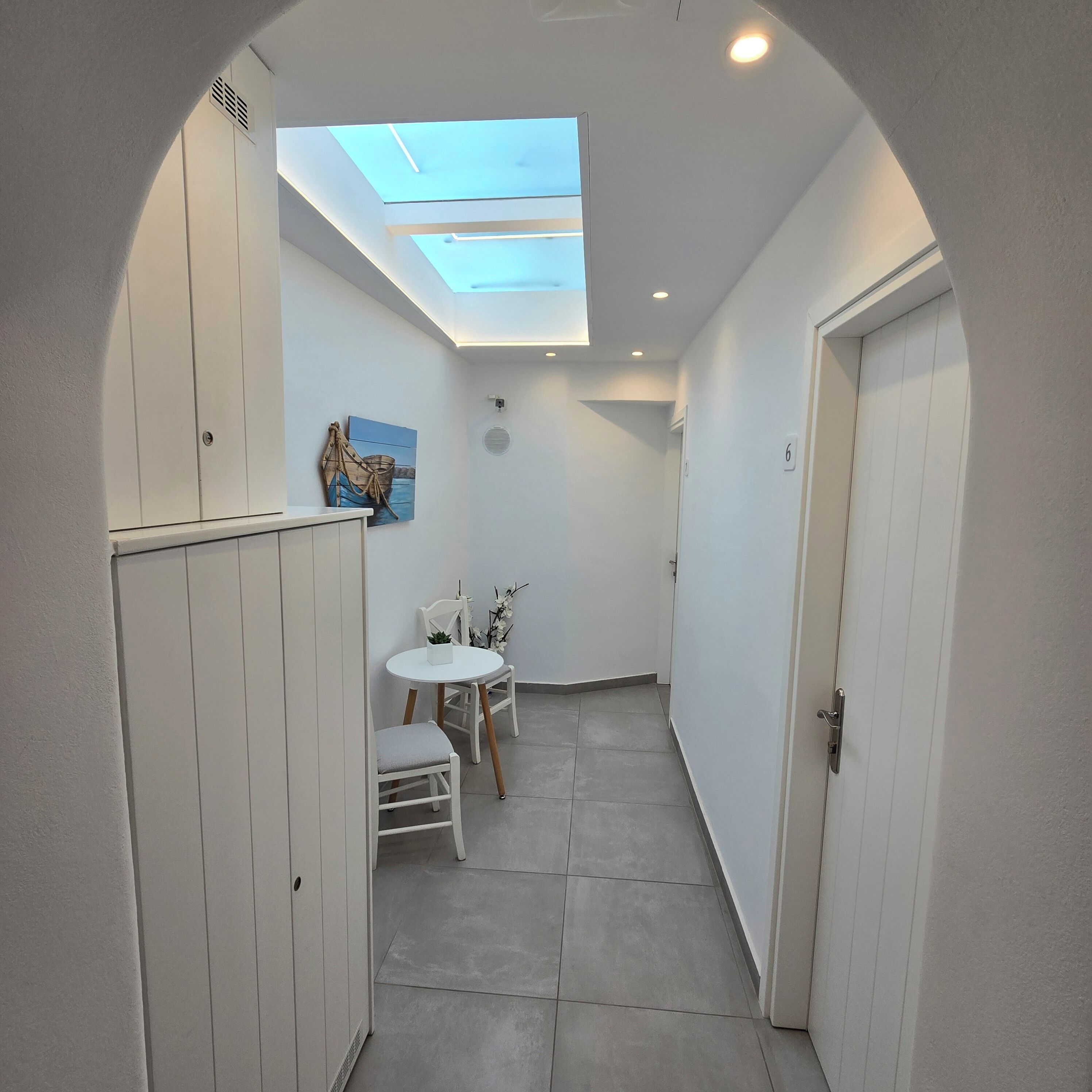 A narrow hallway with a skylight, a small table with chairs, and a door marked with the number 6.