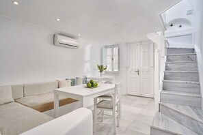 Uma sala de estar moderna, com decoração em tons de branco, incluindo um sofá, uma mesa de jantar com cadeiras e uma escada com degraus de mármore.
