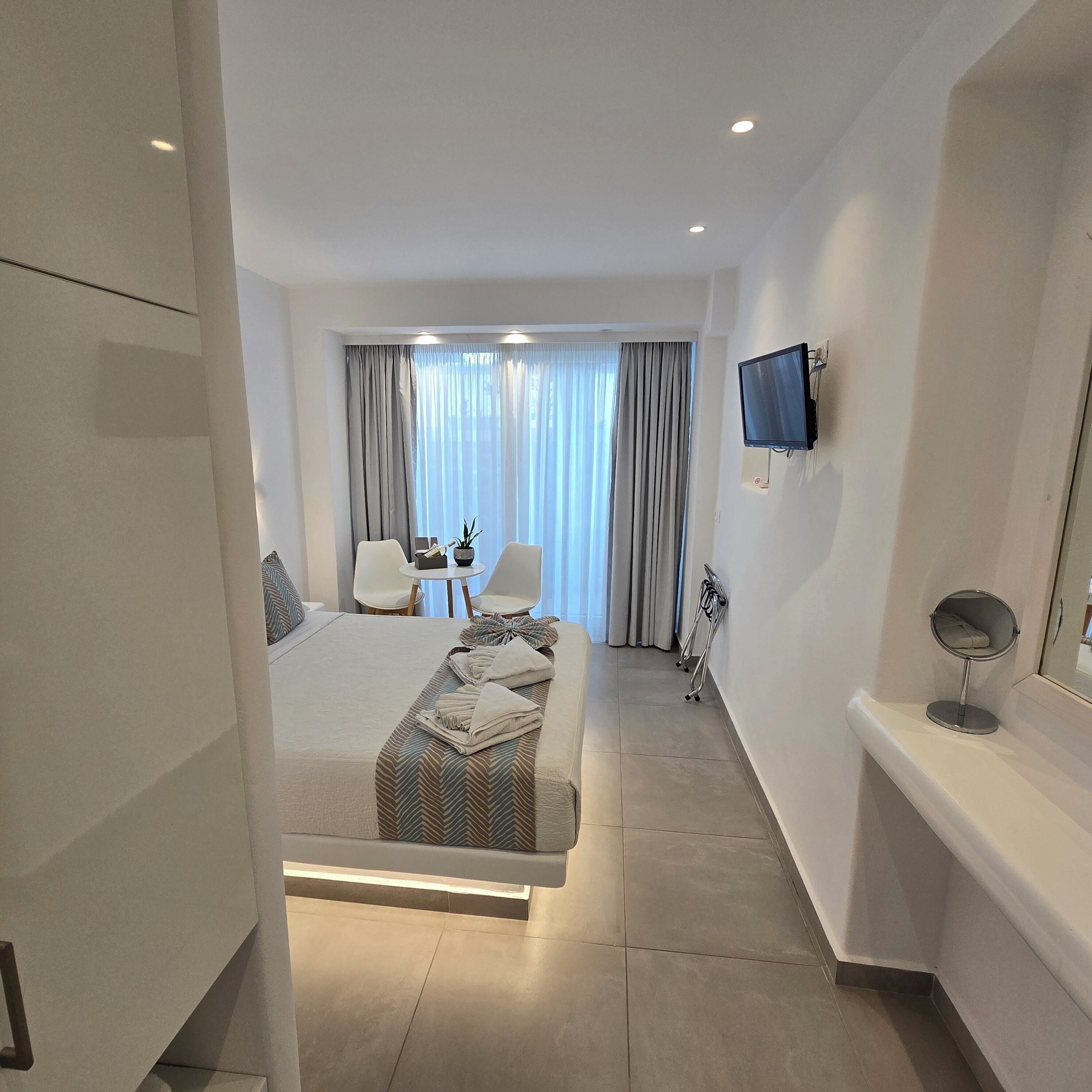 Una habitación de hotel moderna con una cama, un escritorio, una silla, un televisor y un espejo de baño.