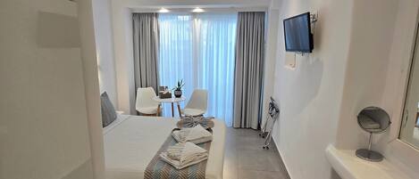 A modern hotel room with a bed, a desk, a chair, a TV, and a bathroom mirror.
