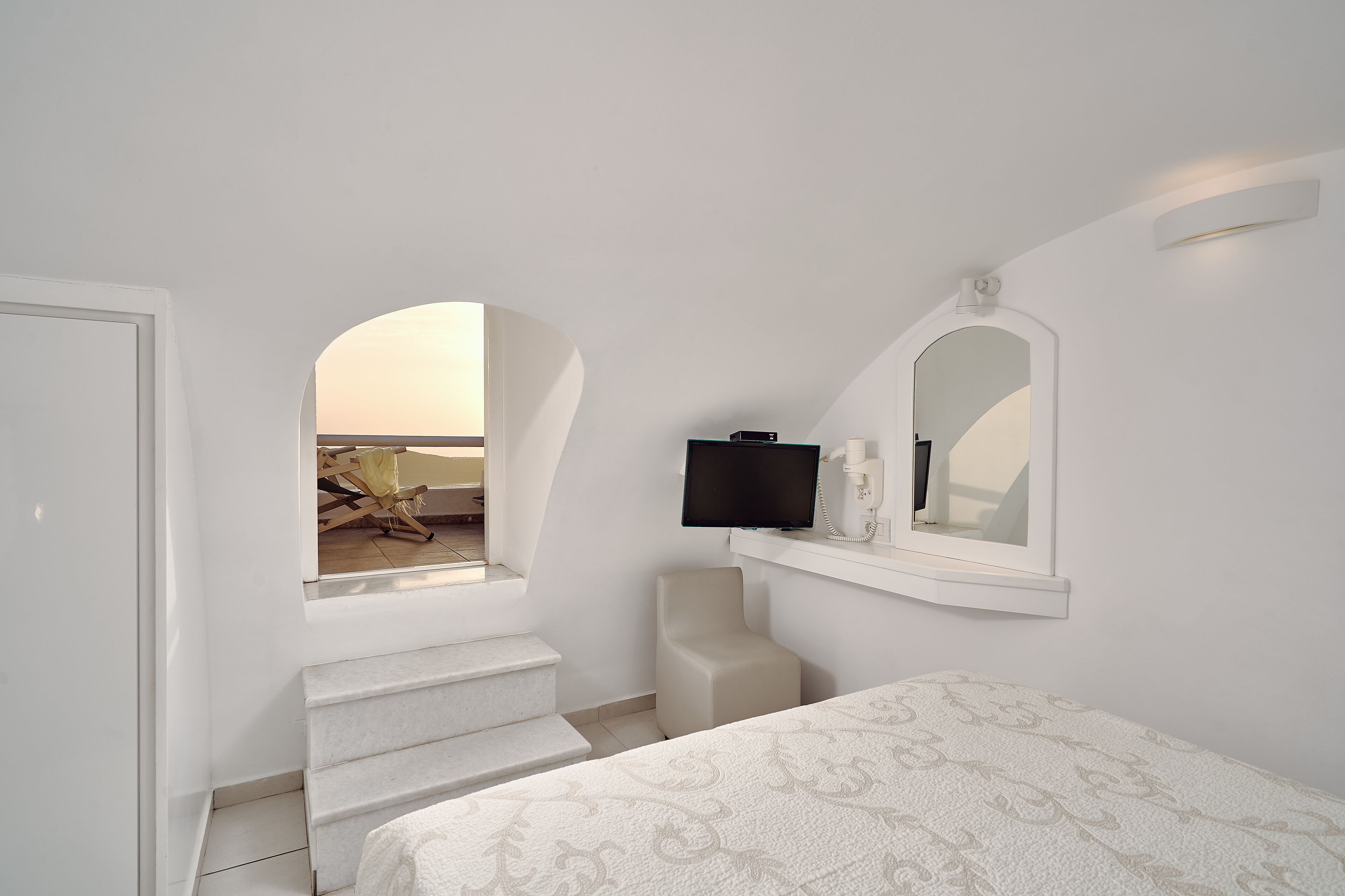 Quarto com cama, televisão, espelho e janela com vista para a praia.