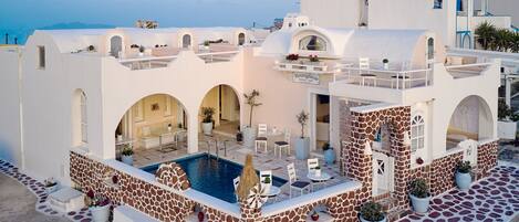 A white building with a pool, outdoor seating, and a view of the sea.