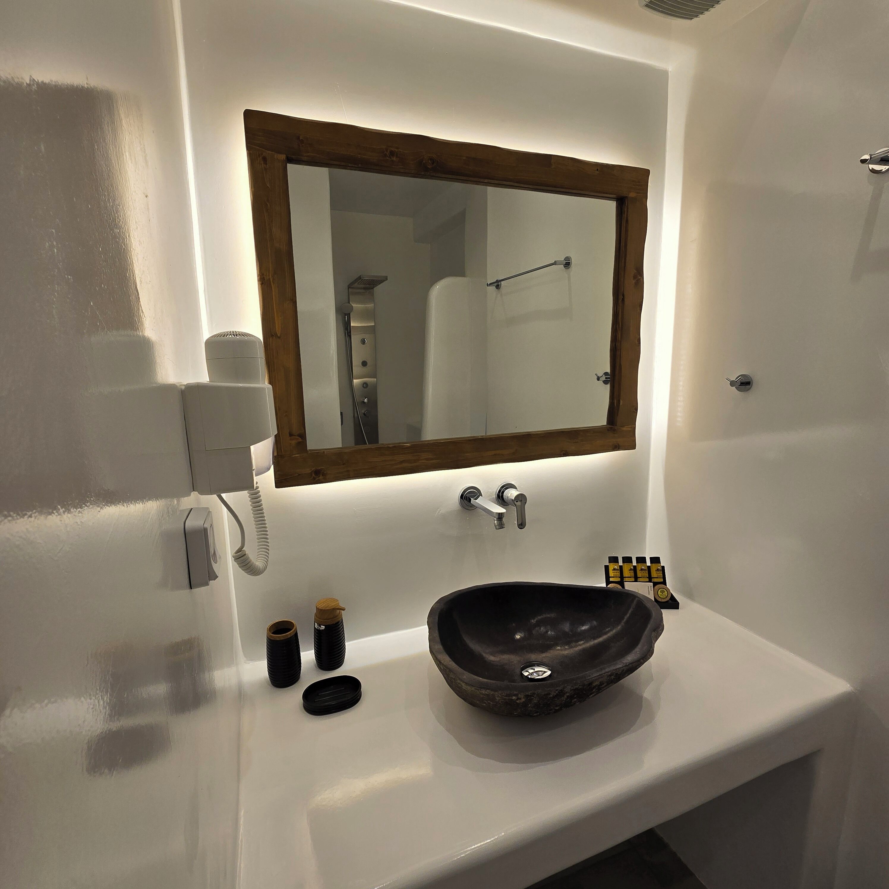 A bathroom with a white sink, a wooden-framed mirror, a white telephone, and a few toiletries.