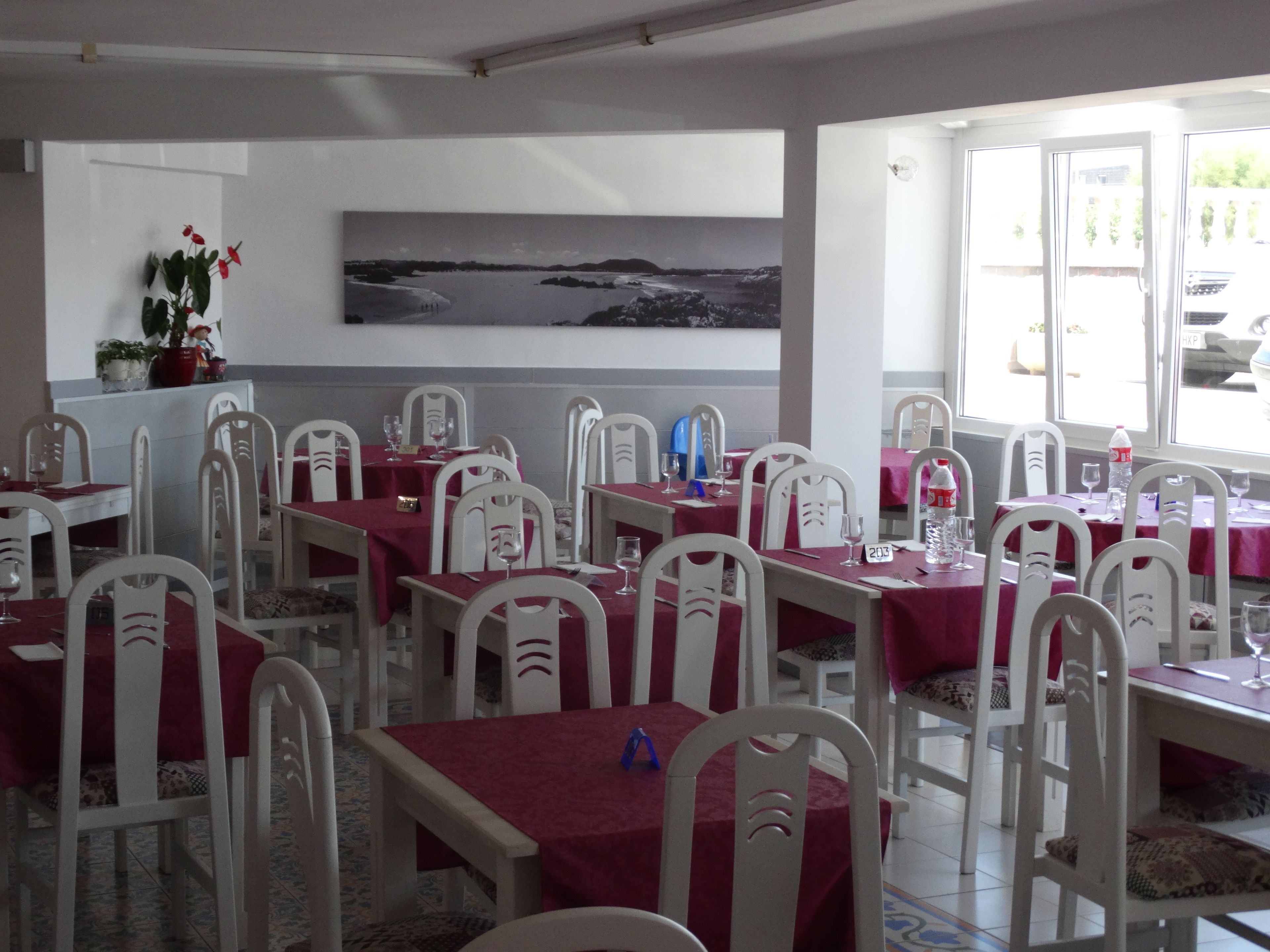 Un comedor con mesas dispuestas para varios comensales, sillas blancas y un cuadro grande en la pared.