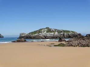 Una playa con un promontorio rocoso y una pequeña colina.
