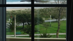 A view through a window with a coastal landscape, including the sea, rocks, and greenery. - Hotel Los Juncos (Noja)