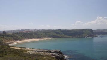 A coastal landscape with a sandy beach, rocky cliffs, and a clear blue sea.