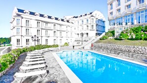 Un gran edificio con piscina, escalones de piedra y sillones de descanso.