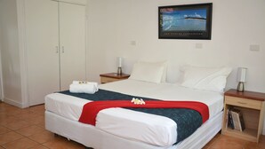 A neatly arranged hotel room with a bed, nightstands, a wardrobe, and a framed picture on the wall. - Base Airlie Beach Resort - Hostel (Airlie Beach)