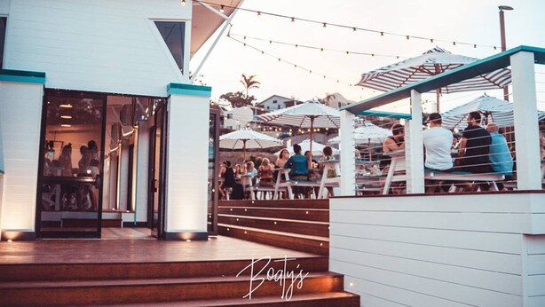 An outdoor seating area with tables and umbrellas, a staircase leading to a building entrance, and string lights. - Base Airlie Beach Resort - Hostel (Airlie Beach)