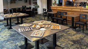 A spacious indoor area with multiple tables and chairs, a bar area with a variety of bottles, and hanging pendant lights. - The Originals City, City Hôtel, Beauvais (Beauvais)