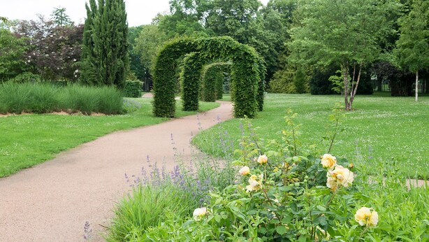 A garden pathway with a central archway surrounded by lush greenery and flowering plants. - The Originals City, City Hôtel, Beauvais (Beauvais)