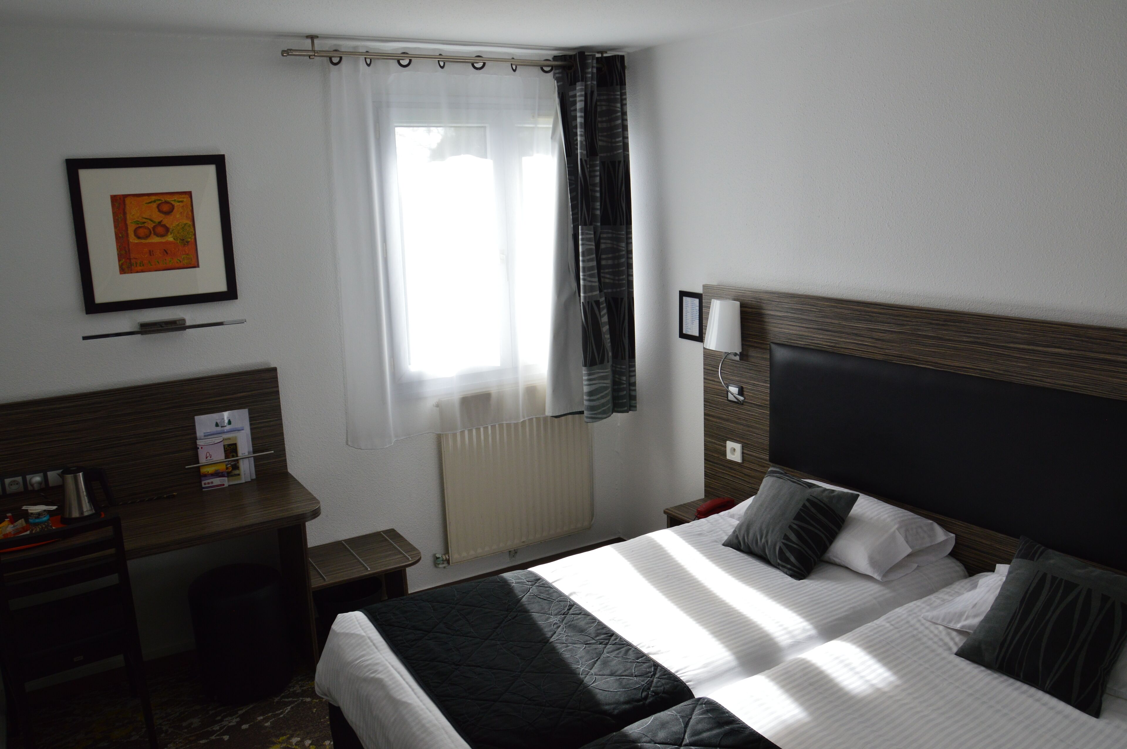 Habitación de hotel con cama, escritorio, silla, radiador y ventana con cortinas.