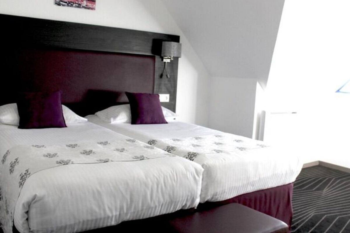A hotel room with a large bed, two pillows, a headboard, and a window.