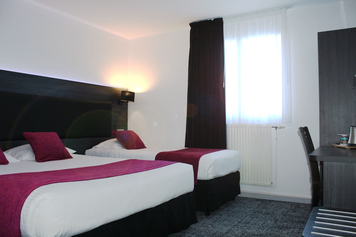 A hotel room with two beds, a desk, and a window with curtains.