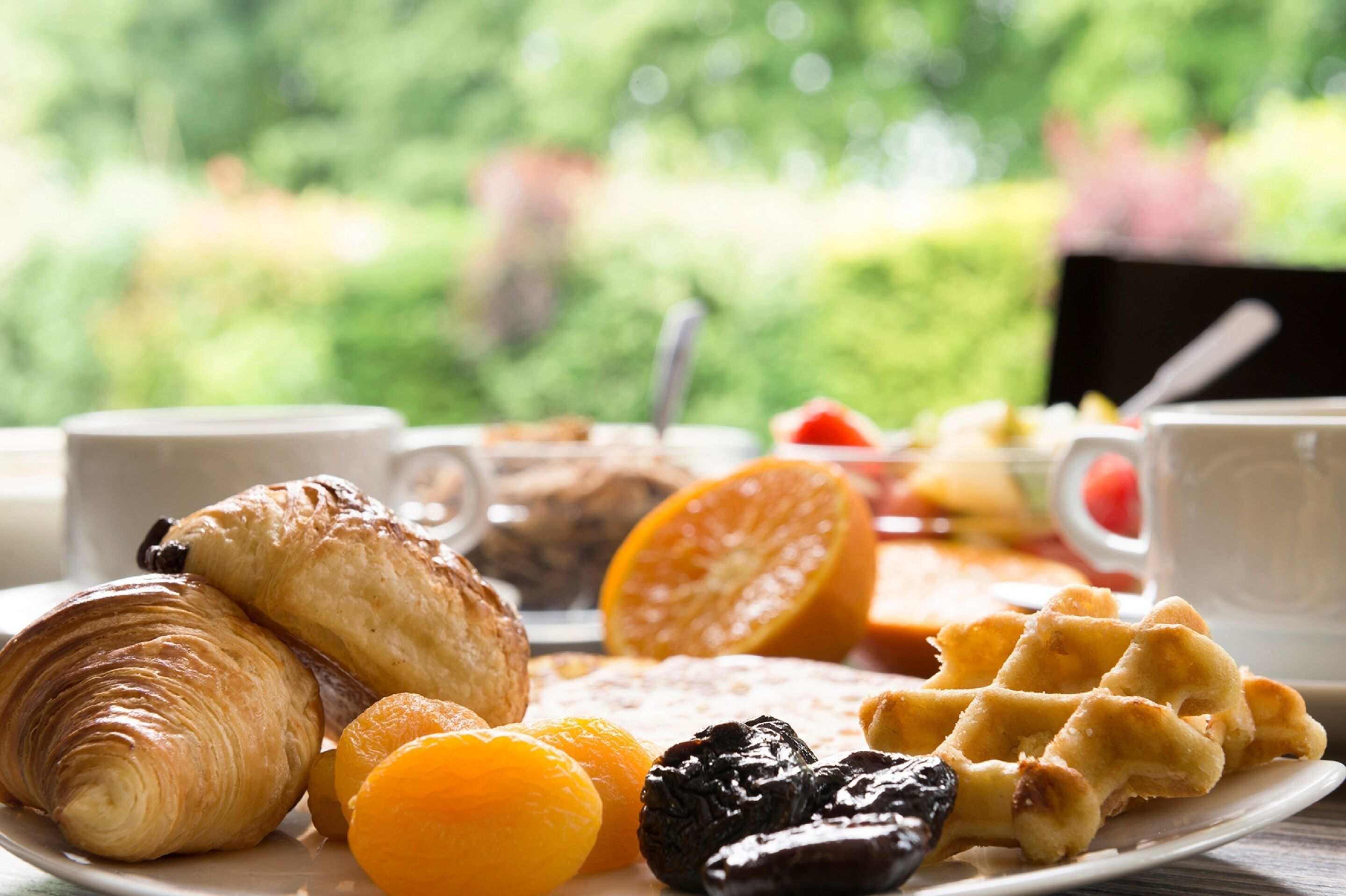 A breakfast plate with croissants, orange slices, and waffles.