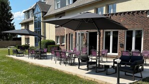 A building with a patio area featuring outdoor seating and umbrellas. - The Originals City, City Hôtel, Beauvais (Beauvais)