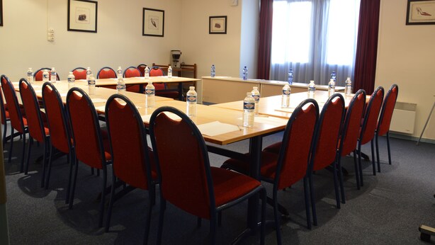 A conference room with a long table, red chairs, and water bottles on the table.