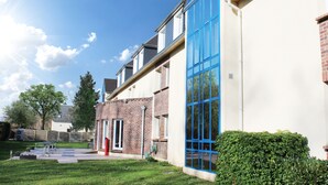 A building with a brick facade and large blue windows, a door, and a well-maintained lawn. - The Originals City, City Hôtel, Beauvais (Beauvais)