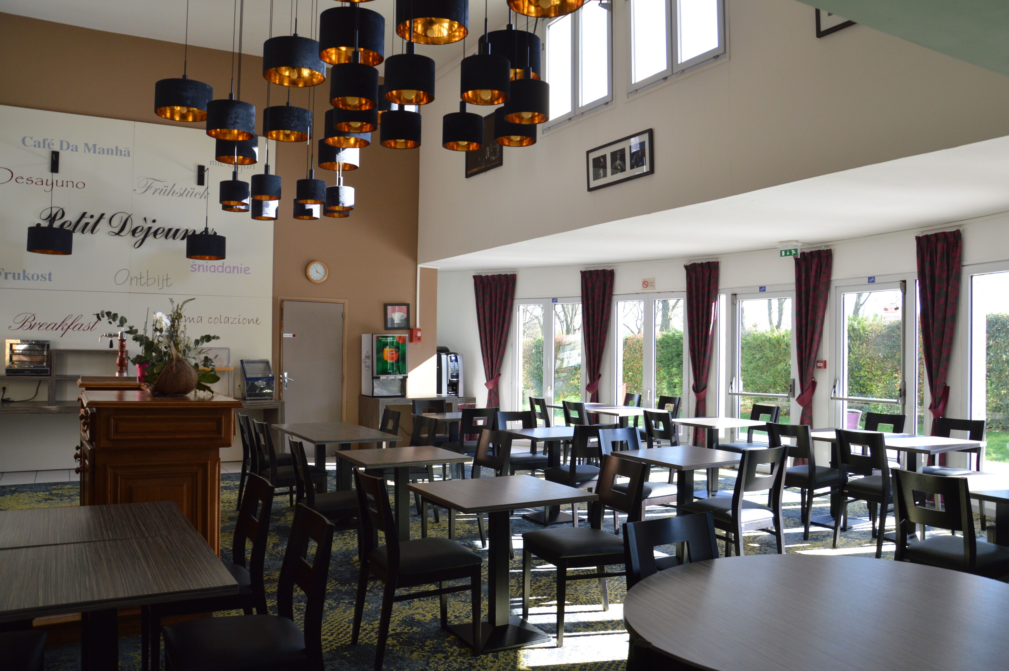 A dining area with multiple tables and chairs, a coffee station, and a large window with curtains.