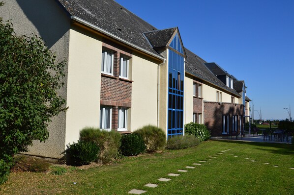 A row of residential buildings with brick and plaster exteriors, a clear blue sky, and a well-maintained lawn.